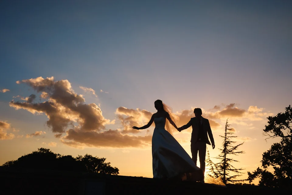 A couple holding hands in silhouette beneath a golden sunset at Kimberley Hall