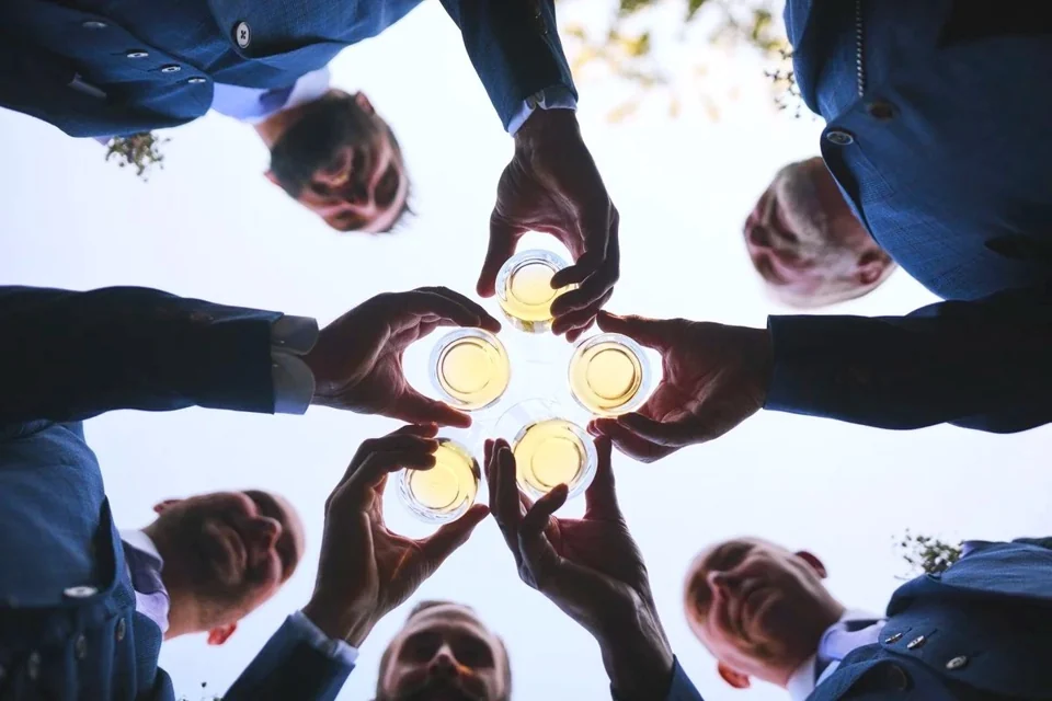 Wedding guests raising their drinks in a circle, photographed from below at The Norfolk Mead